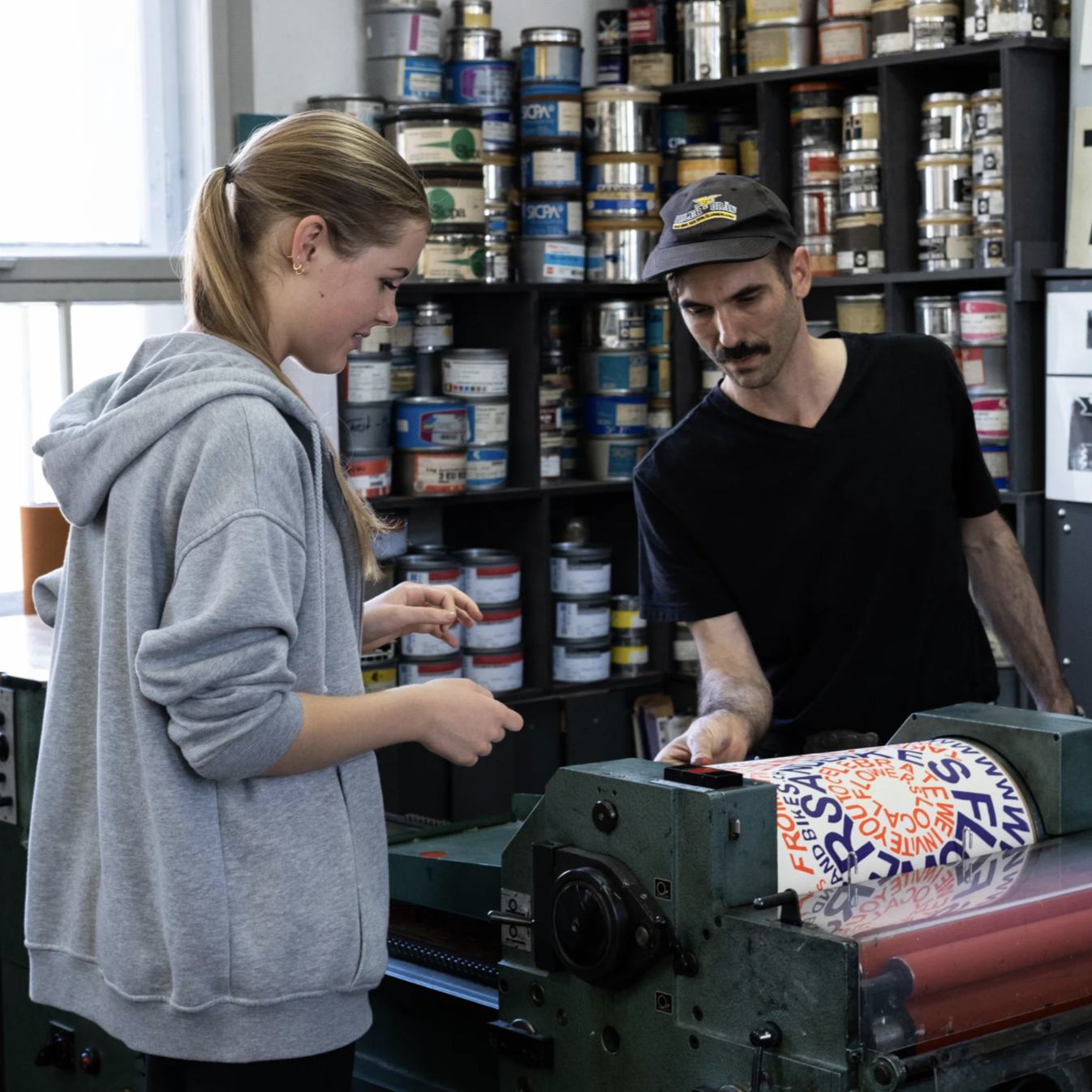 Two people operate an antique printing press in an art studio